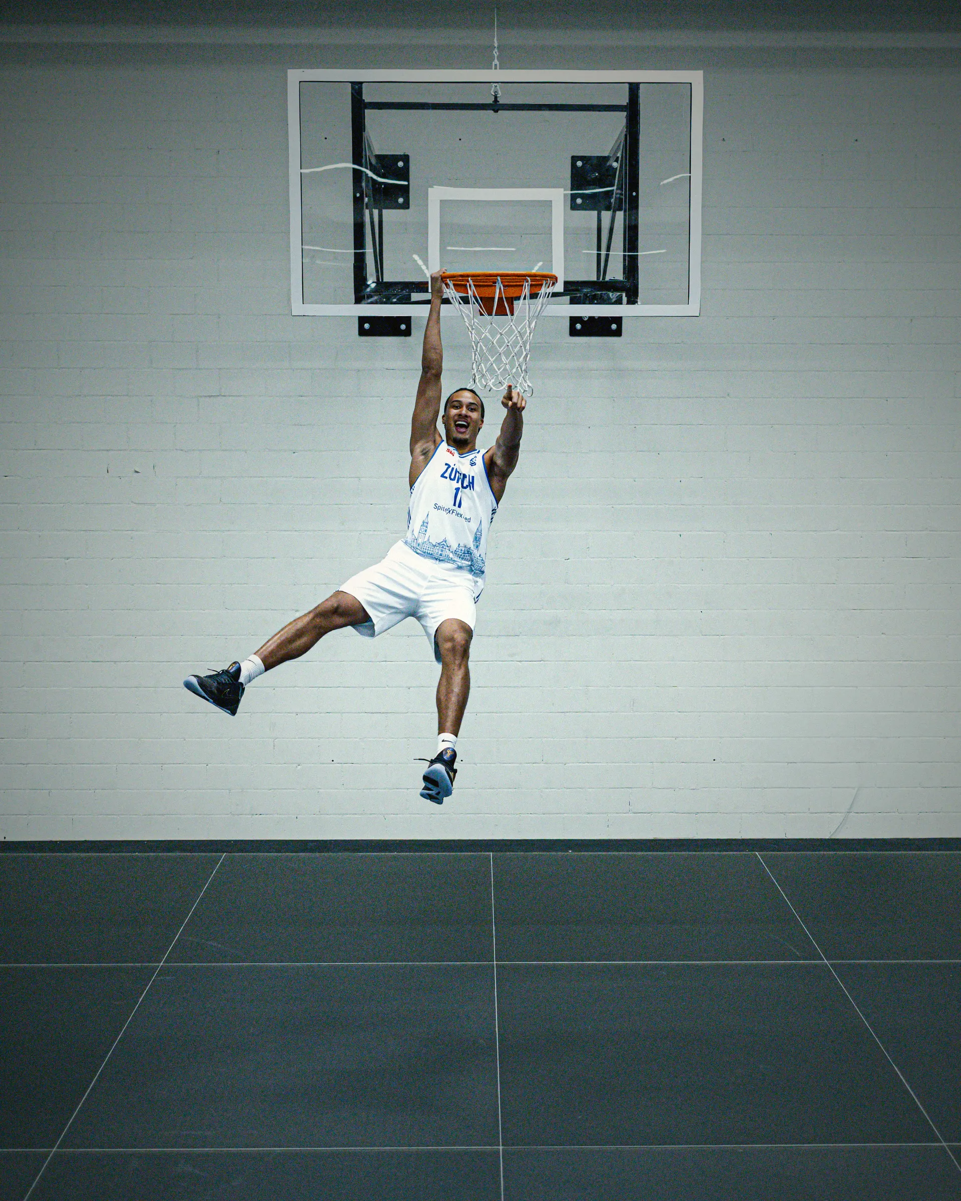 Spieler von GC Basketball hängt nach einem Dunk am Korb, weisses Heimtrikot