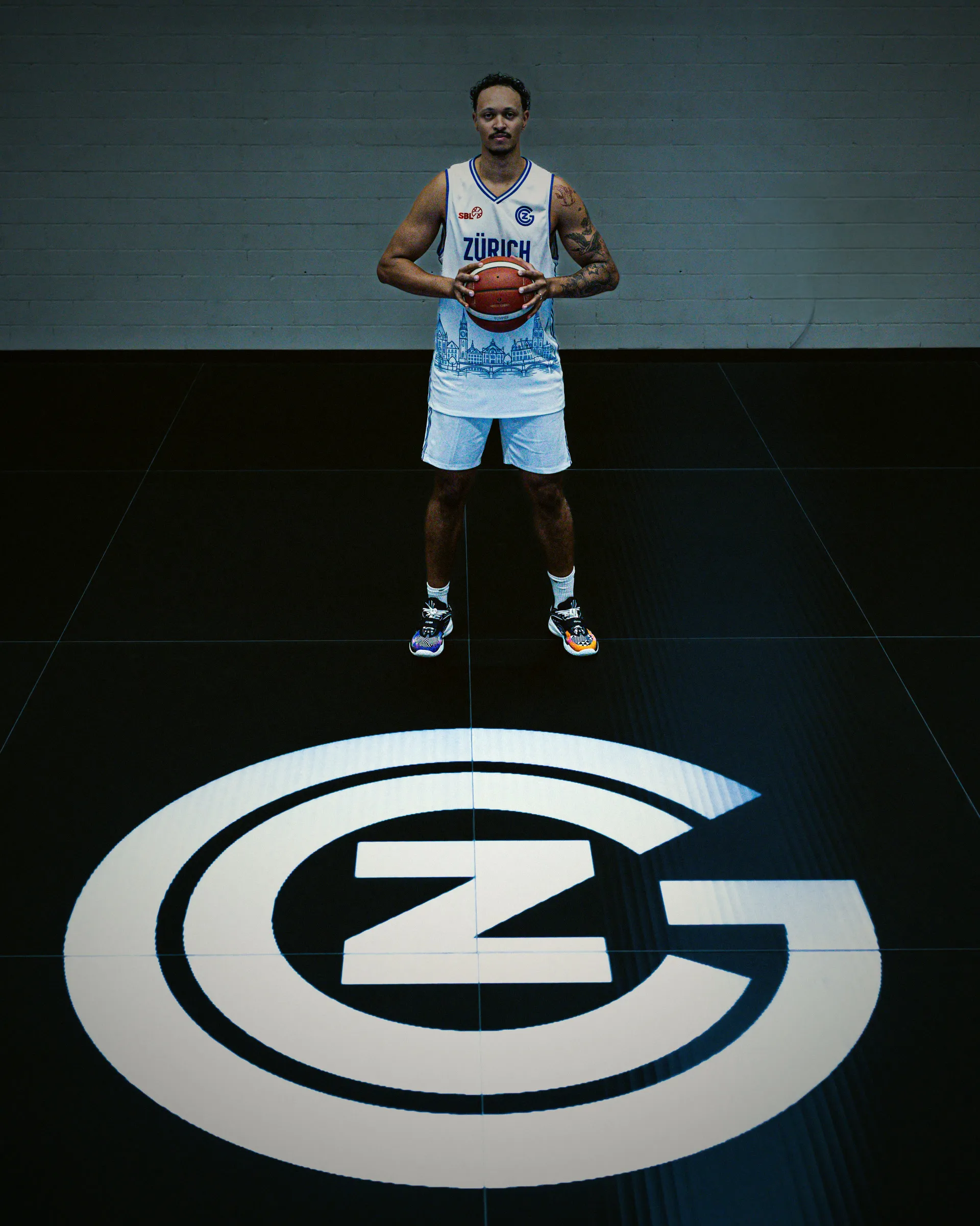 Spieler steht mit dem Ball auf dem beleuchteten GC-Logo im dunklen Studio